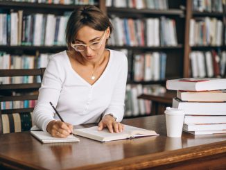 Kobieta robiąca notatki przy biurku w bibliotece, w tle regały z książkami